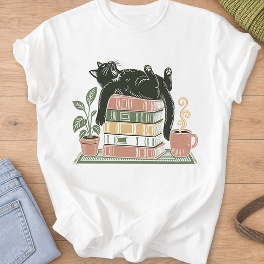 Cat yawning on its back on a stack of books by a potted plant and steaming mug on a White T-Shirt