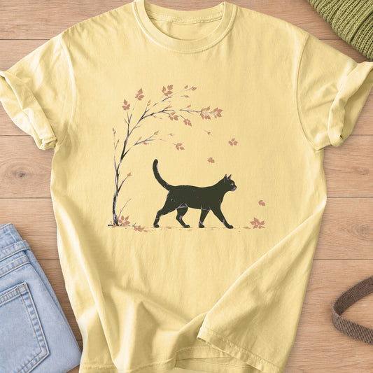 Black cat walking past a slender tree as autumn leaves fall around it on a Butter T-Shirt