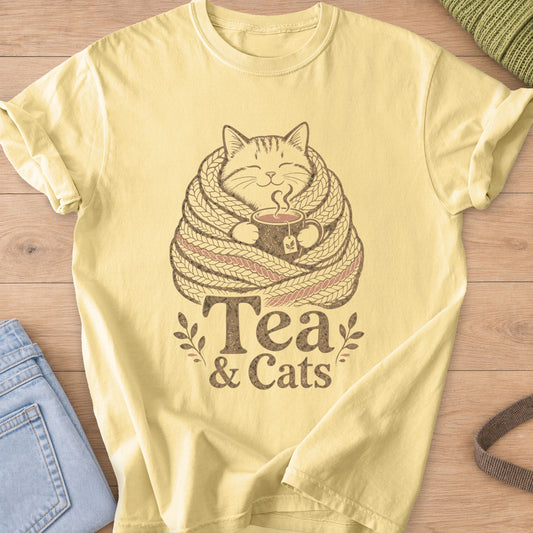Smiling cat wrapped in a knit scarf holding a steaming mug of tea, 'Tea & Cats' on a Butter T-Shirt