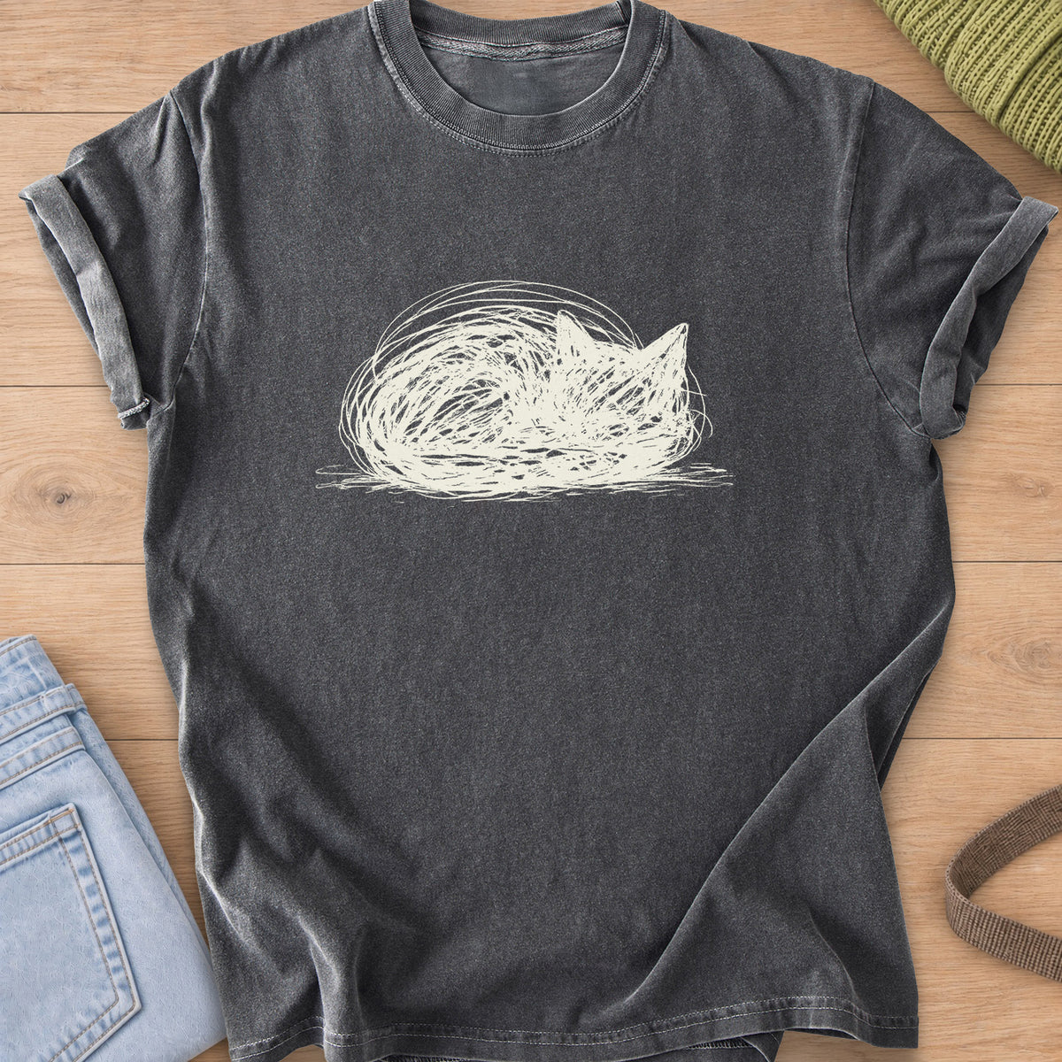 Scribbled cat curled into a round loaf with ears poking up, cream ink on a Pepper T-Shirt
