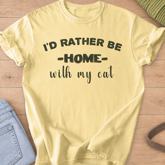 Block letters and script reading "I'D RATHER BE HOME with my cat", dark charcoal ink on a Butter T-Shirt