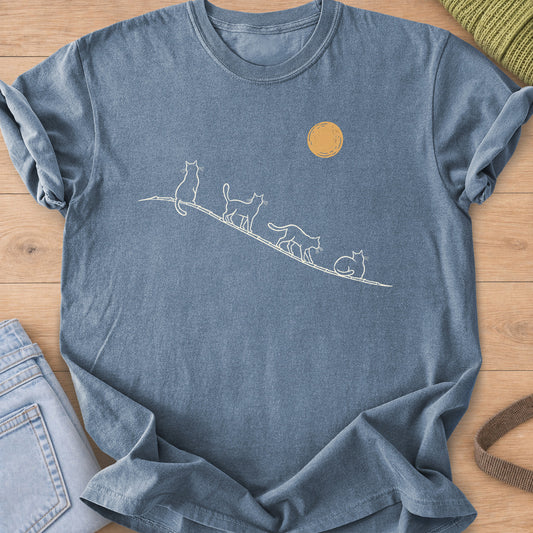 Four cats sit, walk and curl up along a sloping rooftop under a full moon, cream and gold ink on a Blue Jean T-Shirt