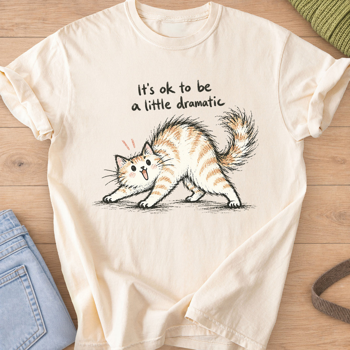 Startled fluffy cat arching its back beneath "It's ok to be a little dramatic" on an Ivory T-Shirt