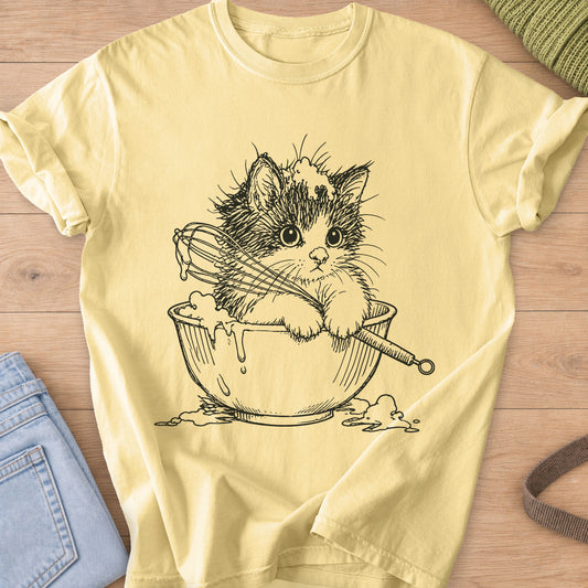 Fluffy kitten in a mixing bowl holding a whisk, with batter dripping over the side, black ink on a Butter T-Shirt