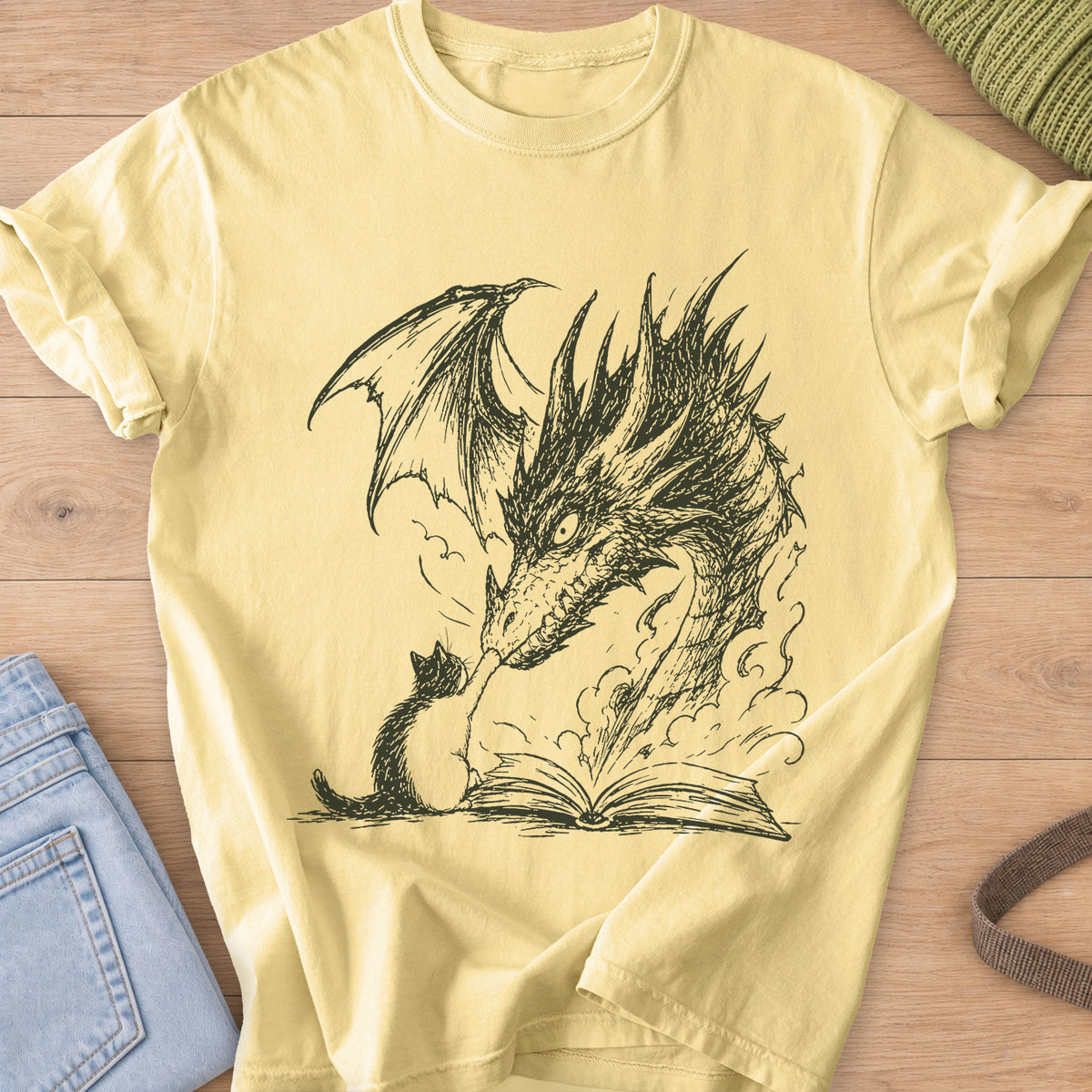 Small cat reaching up to a winged dragon's snout over an open book with smoke, dark charcoal ink on a Butter T-Shirt