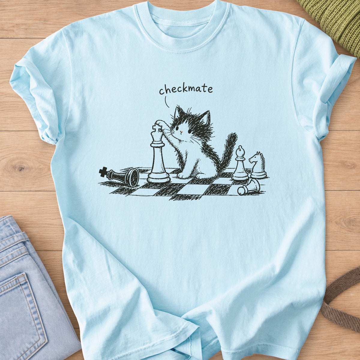 Fluffy kitten with a paw on a chess king, toppled pieces on a board, "checkmate", dark charcoal ink on a Chambray T-Shirt