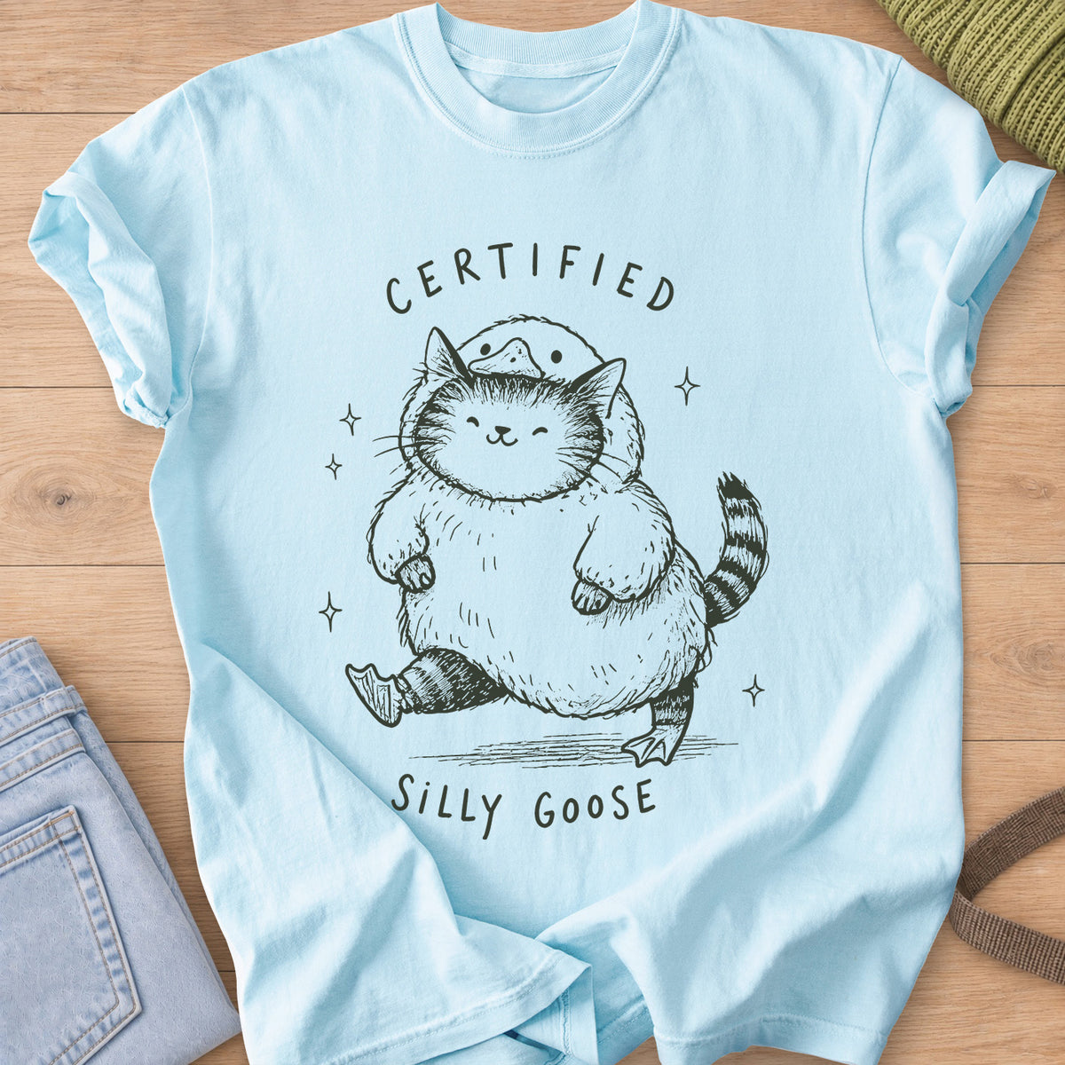 Chubby tabby cat in a goose costume walking among sparkles, "Certified Silly Goose", dark charcoal ink on a Chambray T-Shirt