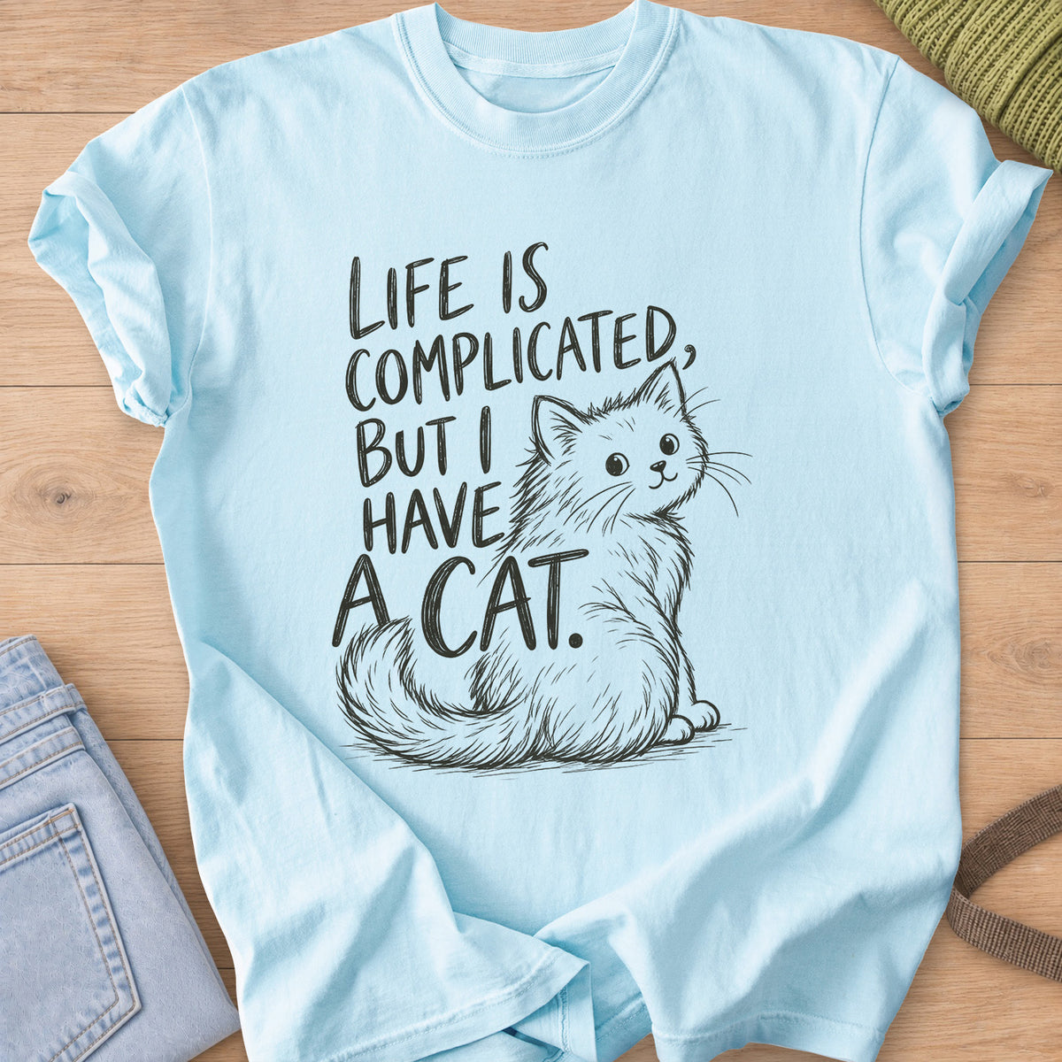 Fluffy cat sits and looks back beside "Life is complicated, but I have a cat.", dark charcoal ink on a Chambray T-Shirt
