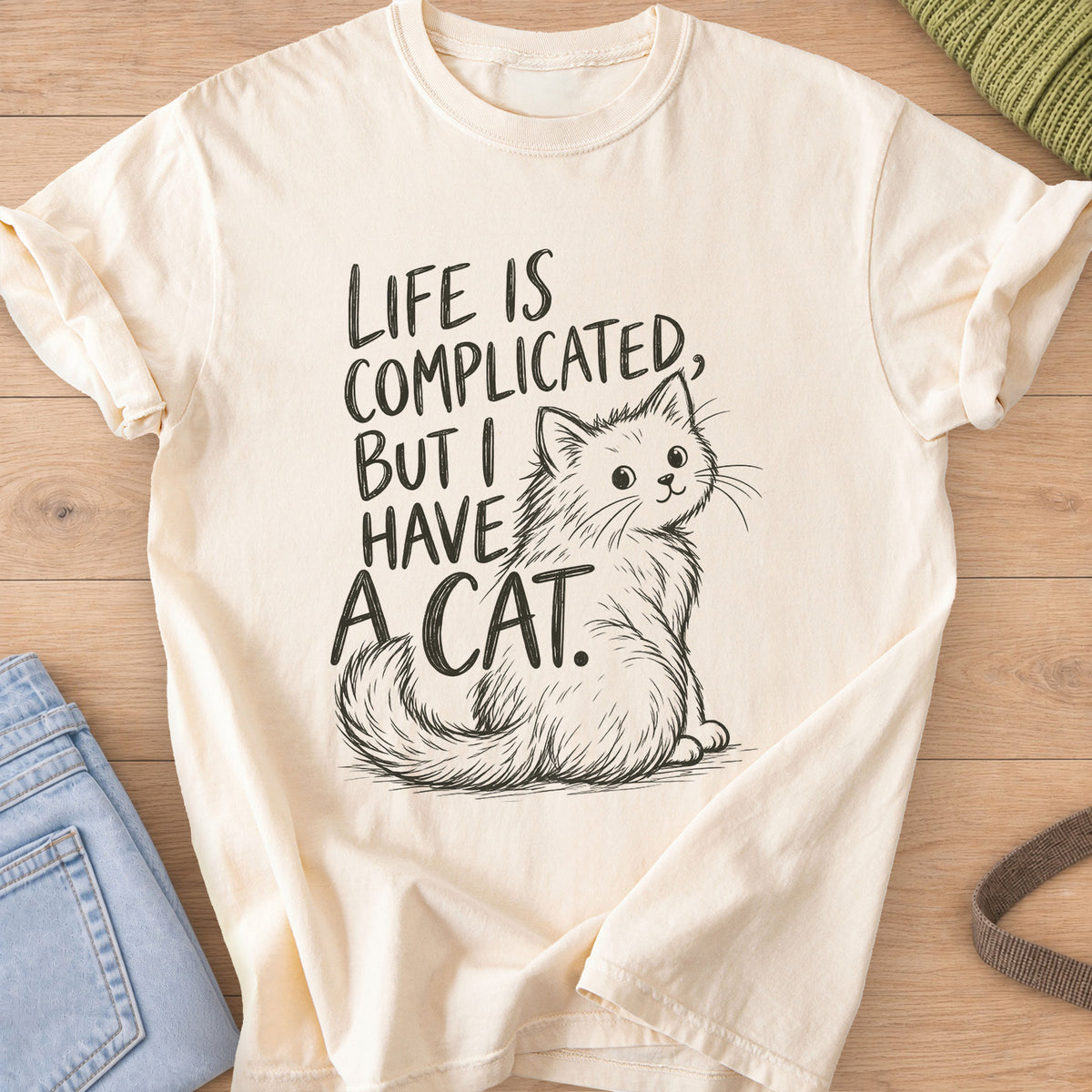 Fluffy cat sits and looks back beside "Life is complicated, but I have a cat.", dark charcoal ink on an Ivory T-Shirt