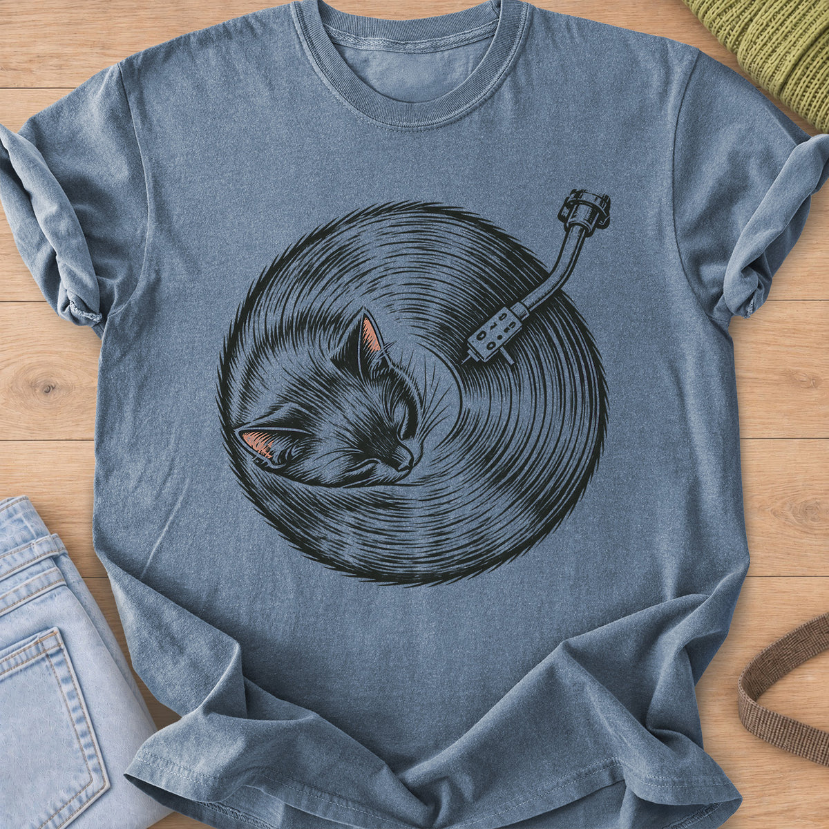 Sleeping cat curled up, its fur forming a vinyl record under a turntable arm, dark charcoal ink on a Blue Jean T-Shirt
