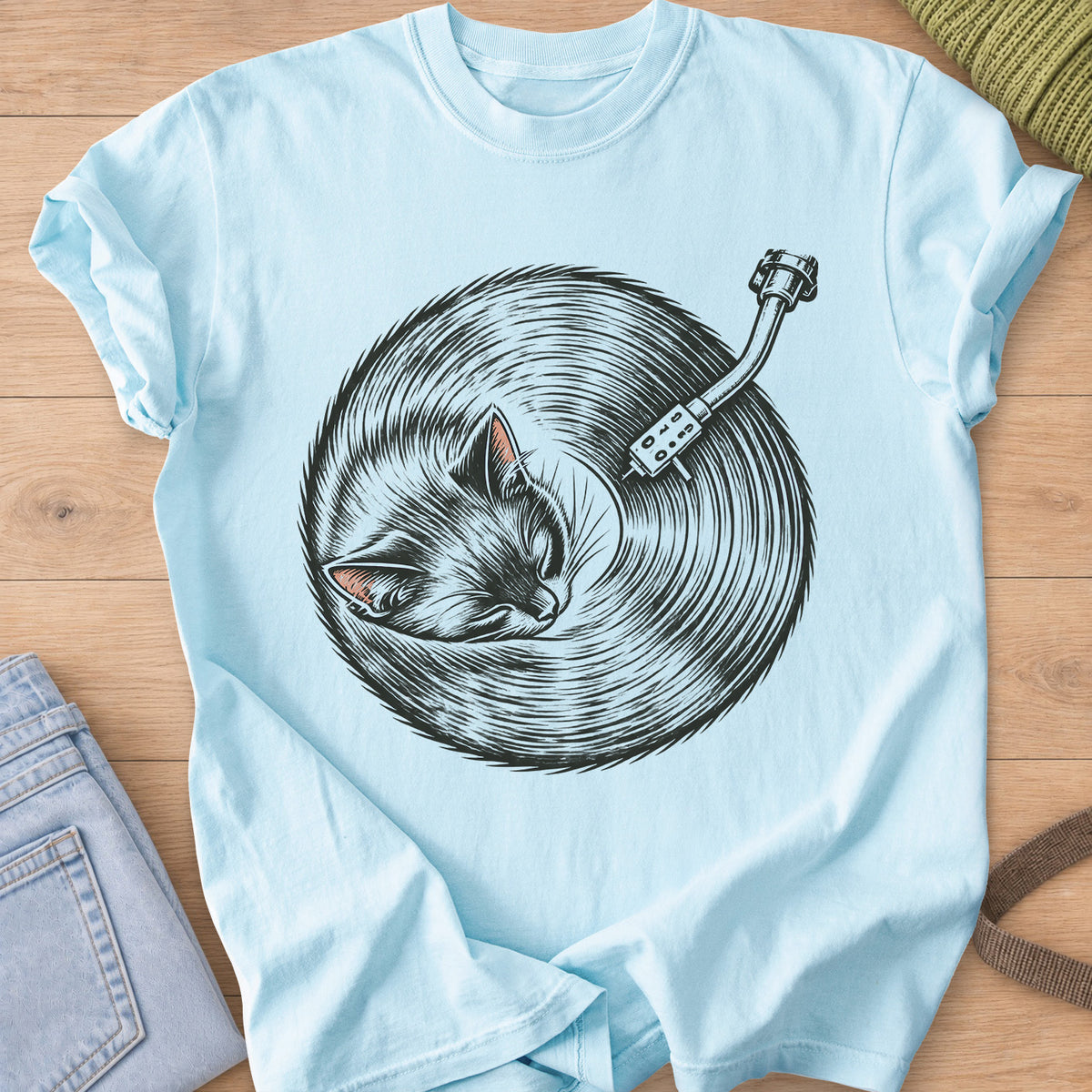 Sleeping cat curled up, its fur forming a vinyl record under a turntable arm, dark charcoal ink on a Chambray T-Shirt
