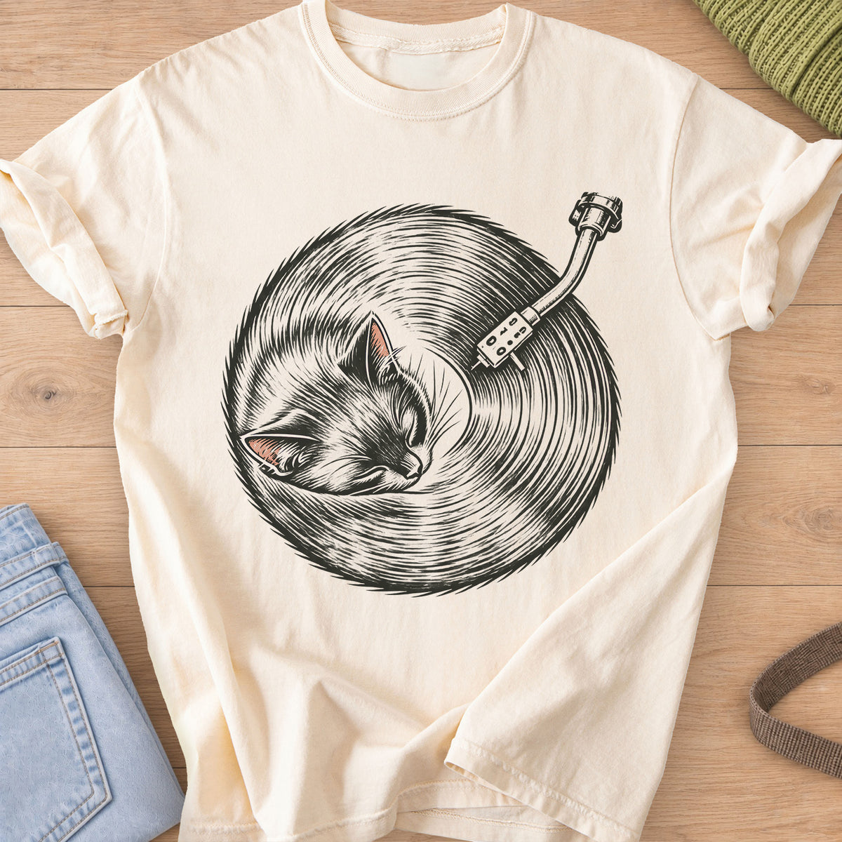 Sleeping cat curled up, its fur forming a vinyl record under a turntable arm, dark charcoal ink on an Ivory T-Shirt