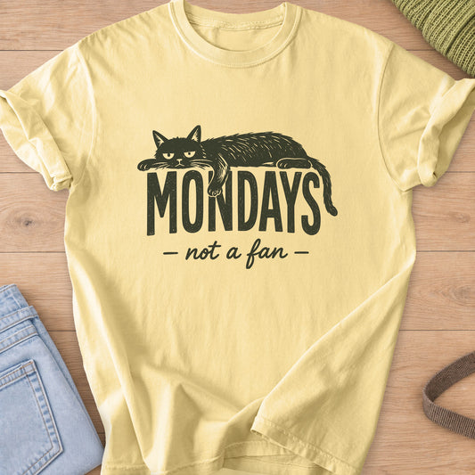 Grumpy cat lying draped over the word "Mondays" with "not a fan" in script below, dark charcoal ink on a Butter T-Shirt