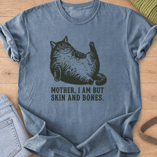 Chubby fluffy cat lying on its back, one paw raised, above "SKIN AND BONES", dark charcoal ink on a Blue Jean T-Shirt