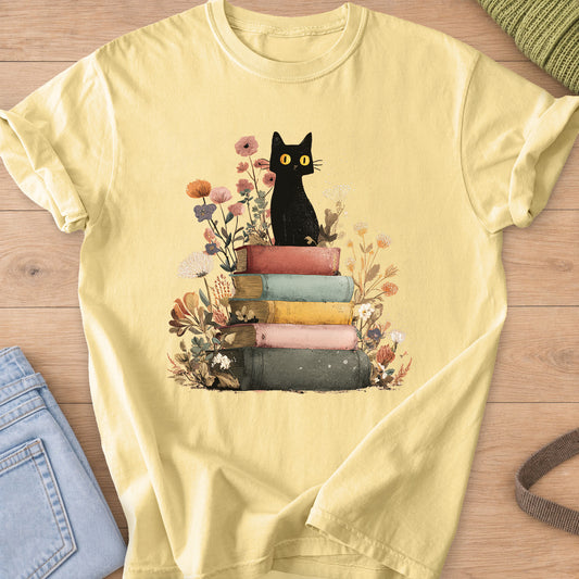 Black cat with yellow eyes sitting on a stack of old books among wildflowers on a Butter T-Shirt