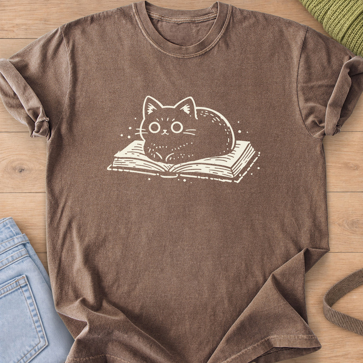 Round cat loaf with wide eyes resting on an open book, small dots around it, cream ink on an Espresso T-Shirt
