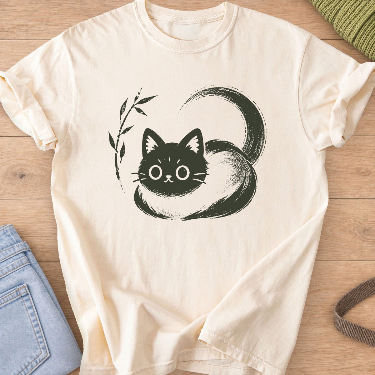 Wide-eyed cat loaf wrapped in a sweeping brushstroke tail beside a bamboo sprig, dark charcoal ink on an Ivory T-Shirt