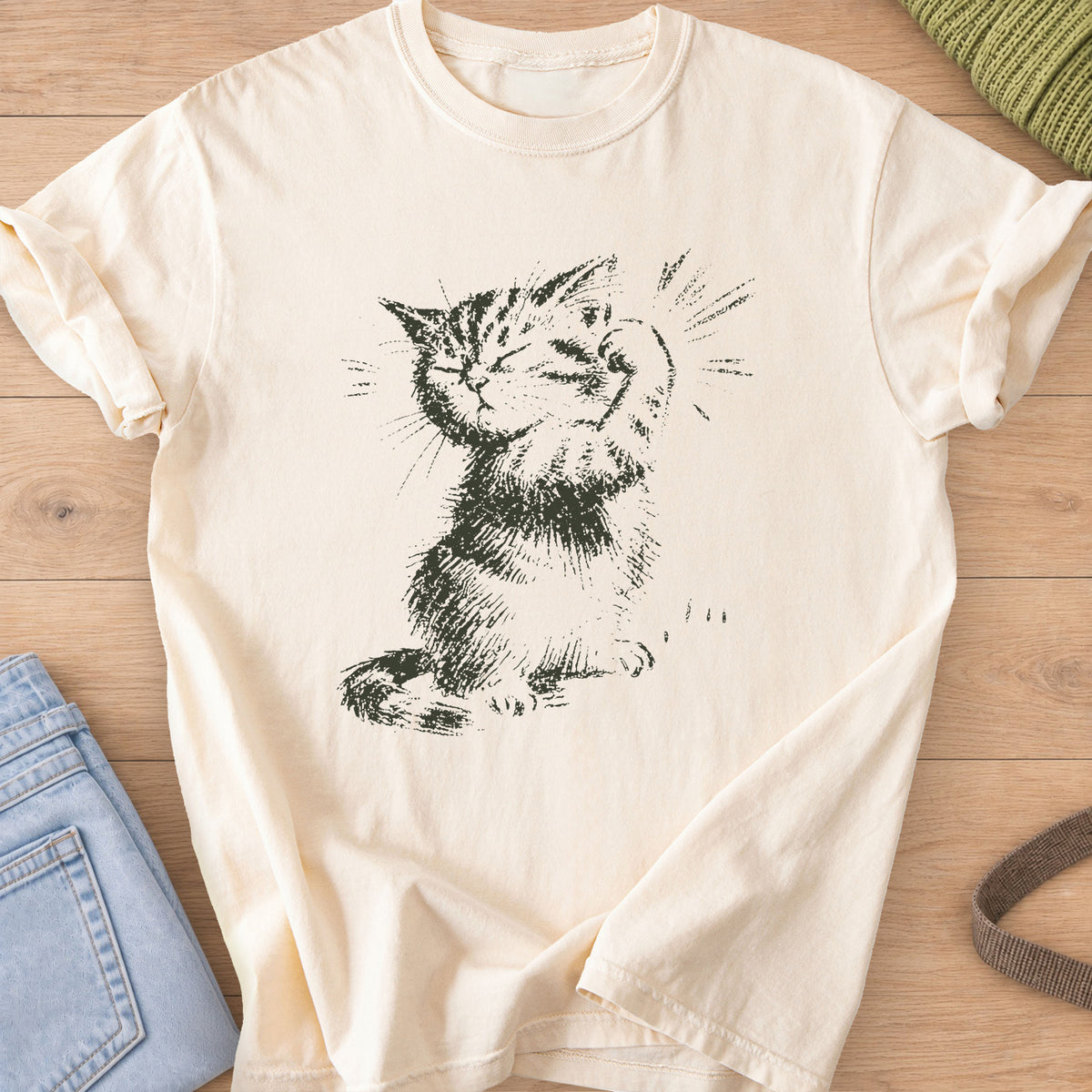 Sketched tabby kitten flexing a raised paw, eyes closed, with burst lines, dark charcoal ink on an Ivory T-Shirt