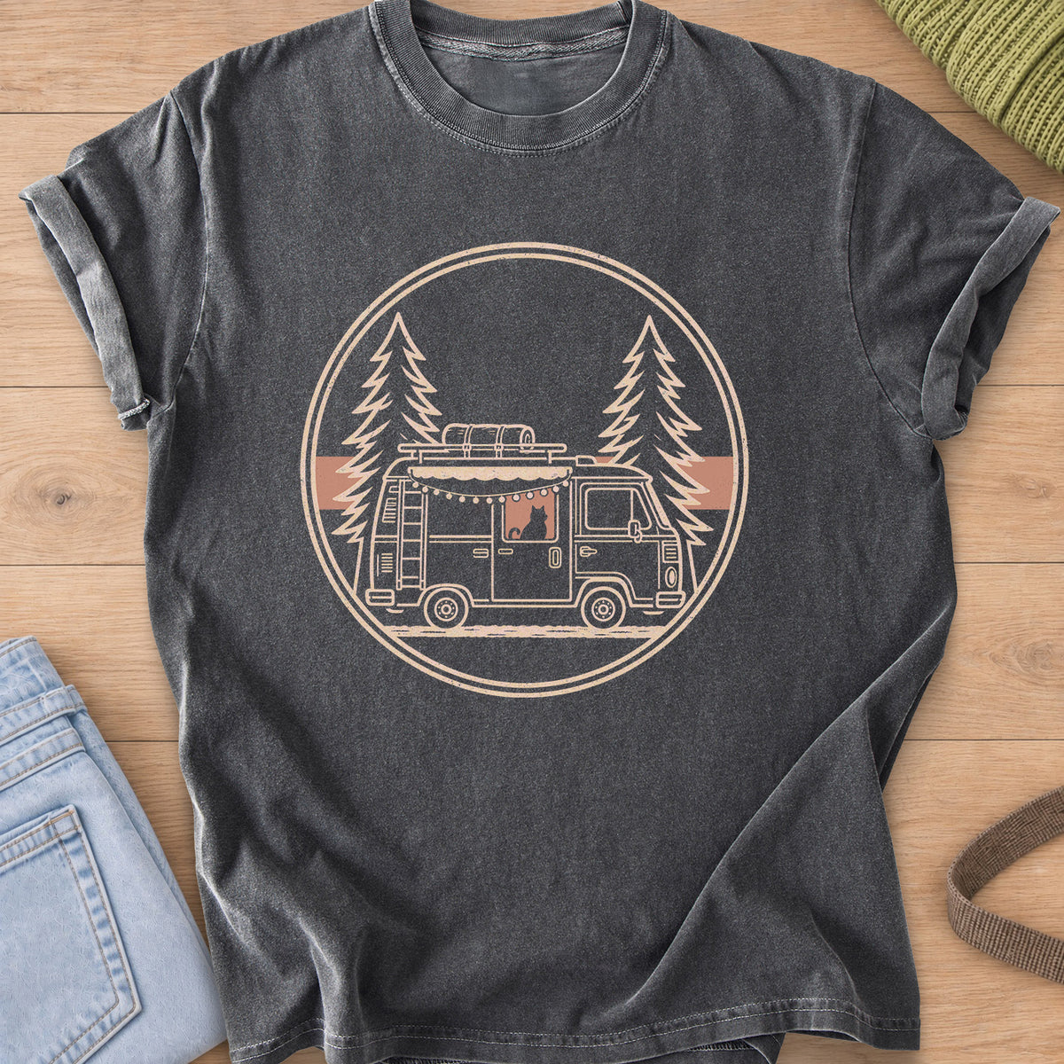 Cat sitting in a camper van window under string lights, framed by pine trees, cream ink on a Pepper T-Shirt