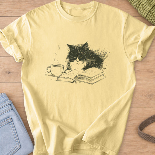 Fluffy tuxedo cat dozing over an open book beside a steaming coffee cup, dark charcoal ink on a Butter T-Shirt