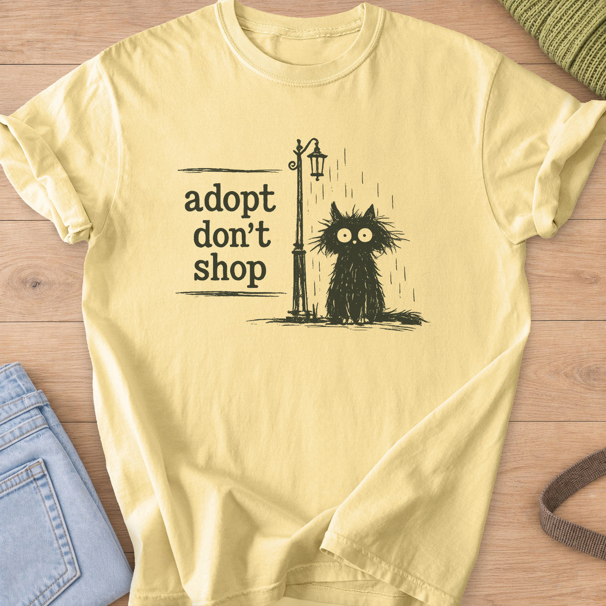 Scruffy black cat sitting in the rain by a street lamp, "adopt don't shop", dark charcoal ink on a Butter T-Shirt