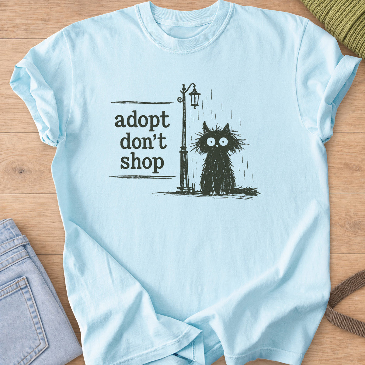 Scruffy black cat sitting in the rain by a street lamp, "adopt don't shop", dark charcoal ink on a Chambray T-Shirt