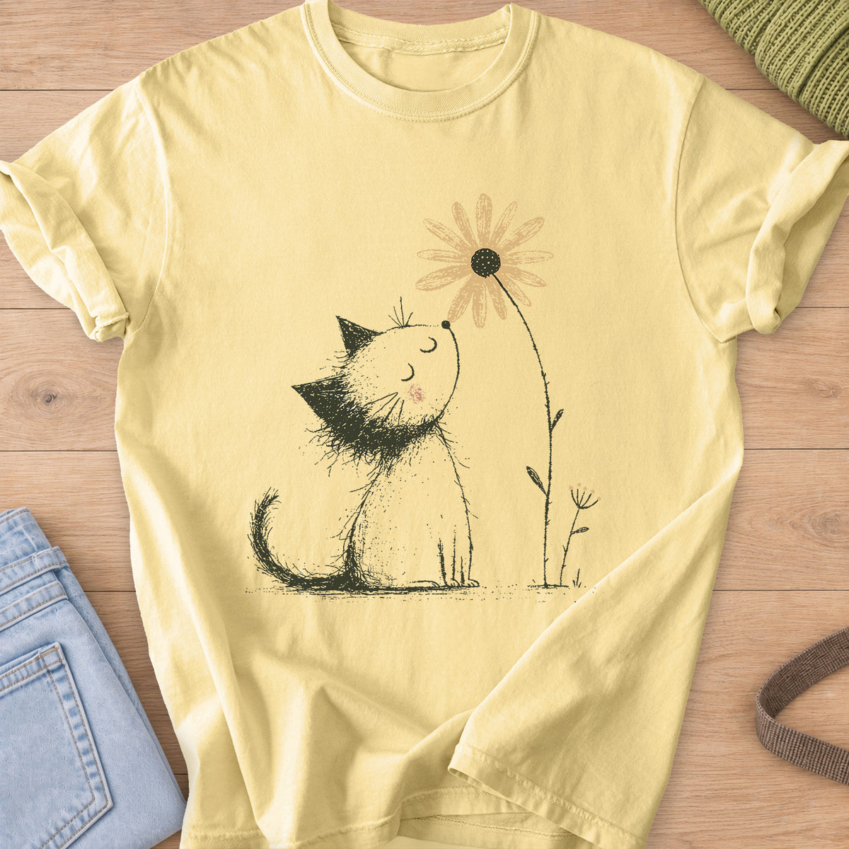 Fluffy kitten with closed eyes and a rosy cheek sniffing a tall daisy on a Butter T-Shirt