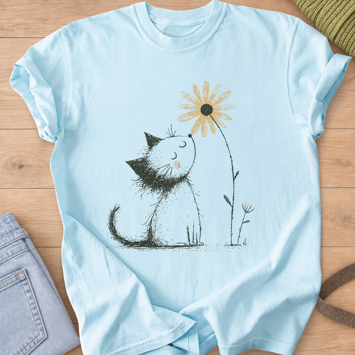 Fluffy kitten with closed eyes and a rosy cheek sniffing a tall daisy on a Chambray T-Shirt