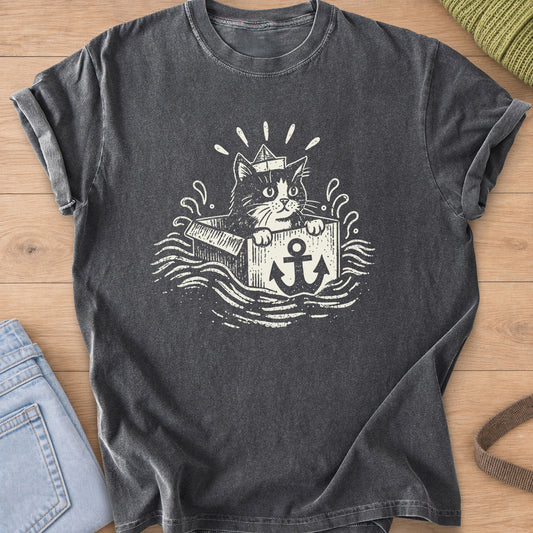 Cat in a paper boat hat peeking from a box with an anchor, floating on waves, cream ink on a Pepper T-Shirt