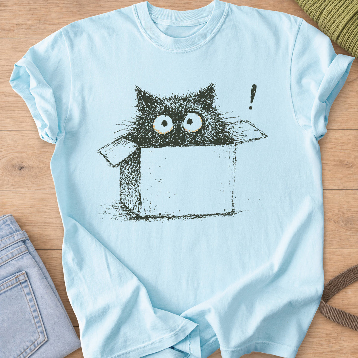 Wide-eyed black cat peeking out of a cardboard box beside an exclamation mark, dark charcoal ink on a Chambray T-Shirt