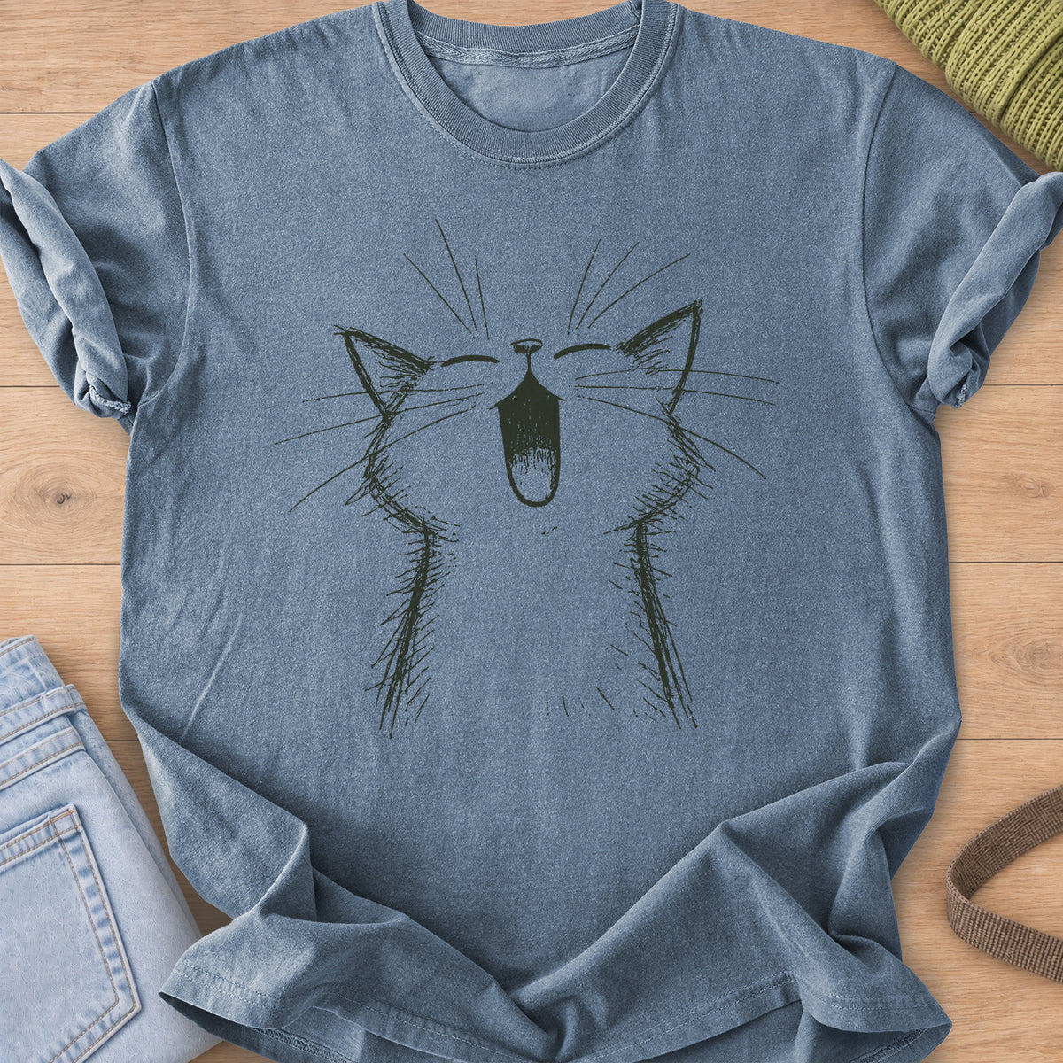 Cat with eyes shut and mouth wide open in a big meow, long whiskers fanning out, dark charcoal ink on a Blue Jean T-Shirt