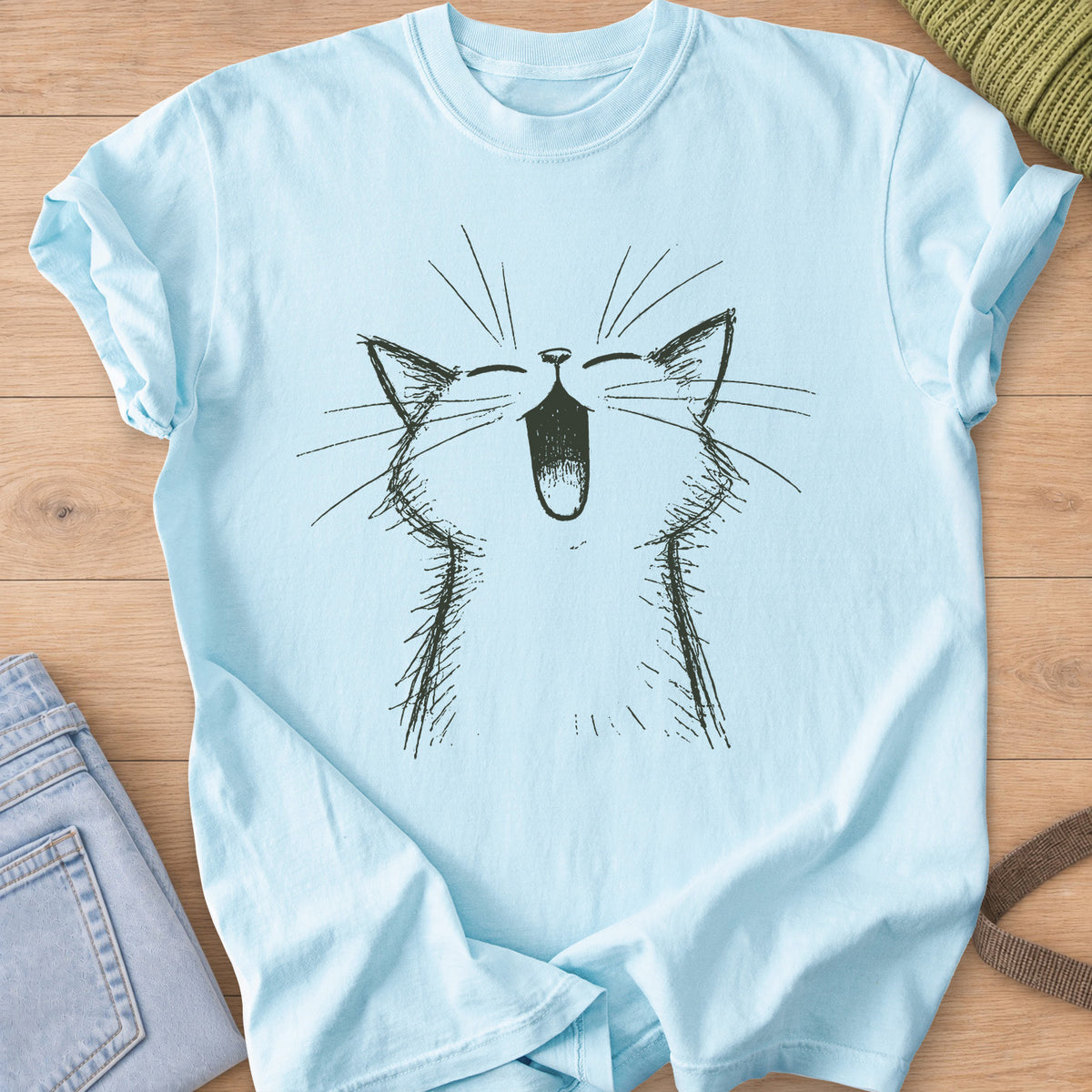 Cat with eyes shut and mouth wide open in a big meow, long whiskers fanning out, dark charcoal ink on a Chambray T-Shirt