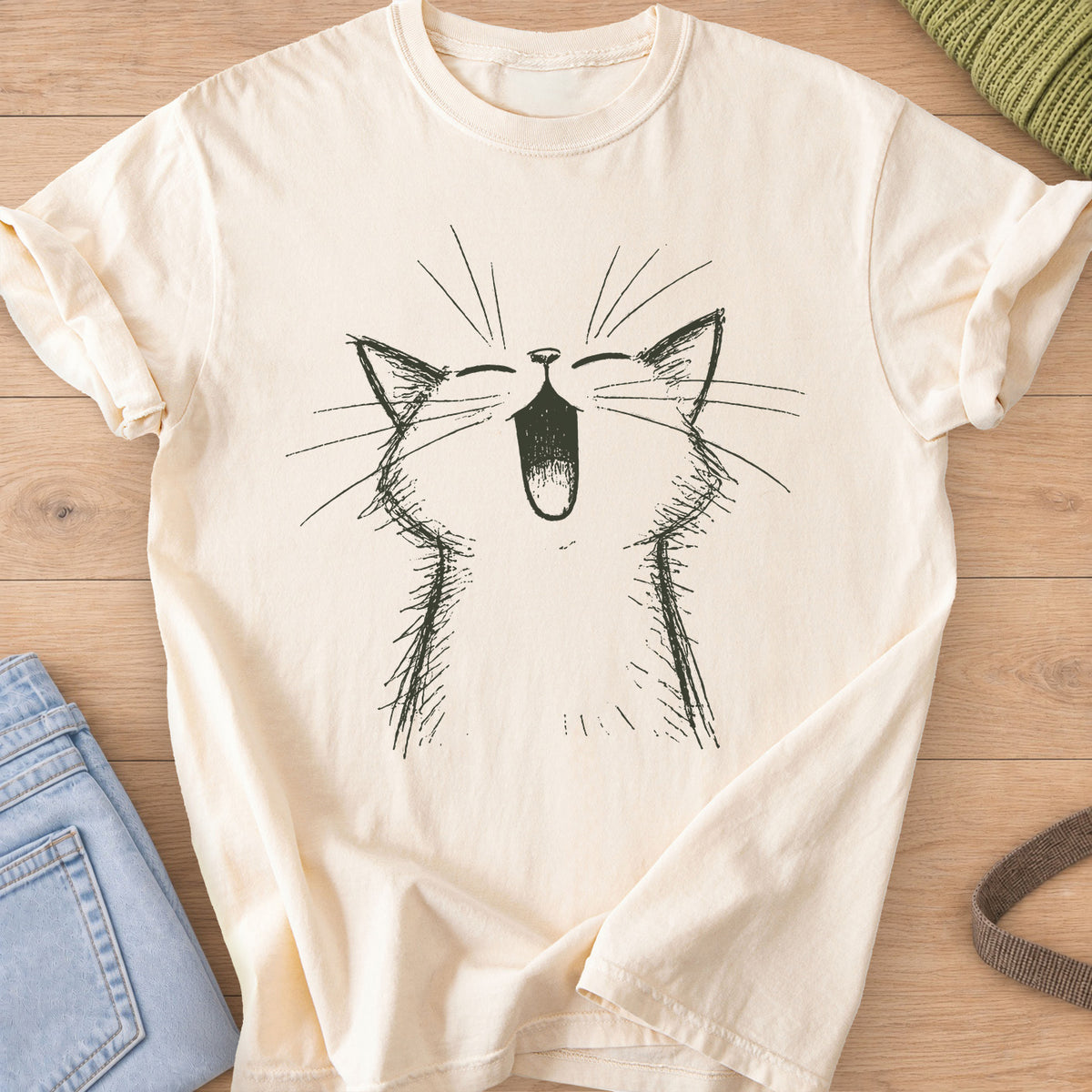 Cat with eyes shut and mouth wide open in a big meow, long whiskers fanning out, dark charcoal ink on an Ivory T-Shirt