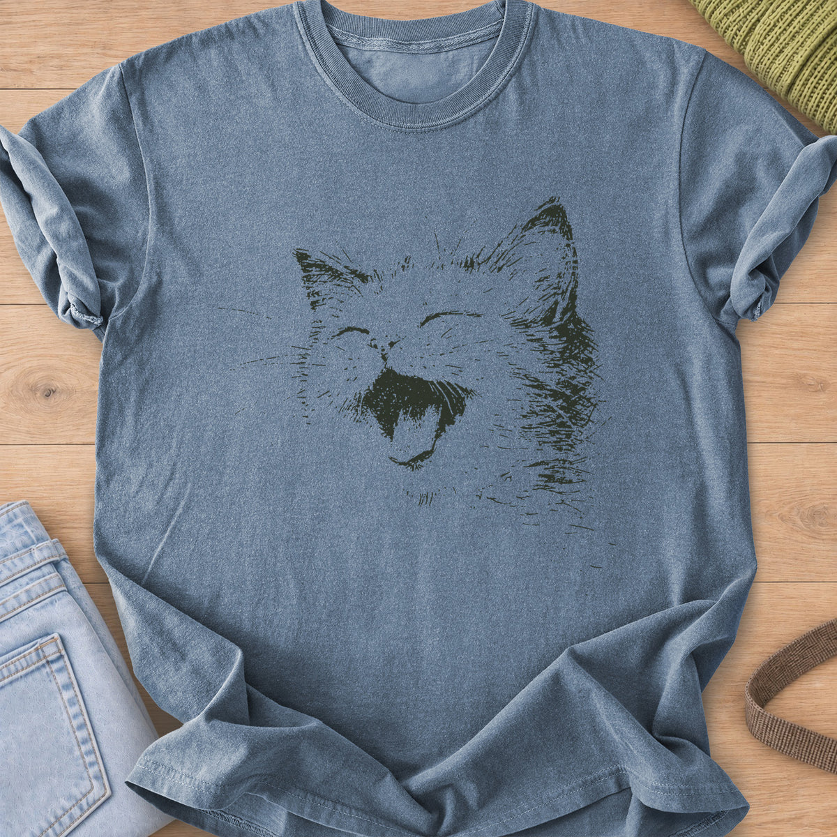 Cat laughing with eyes squeezed shut, mouth wide open and long whiskers, dark charcoal ink on a Blue Jean T-Shirt