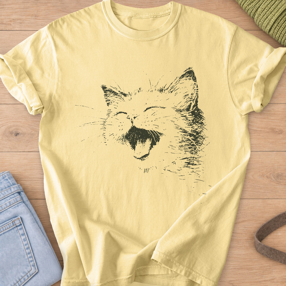 Cat laughing with eyes squeezed shut, mouth wide open and long whiskers, dark charcoal ink on a Butter T-Shirt