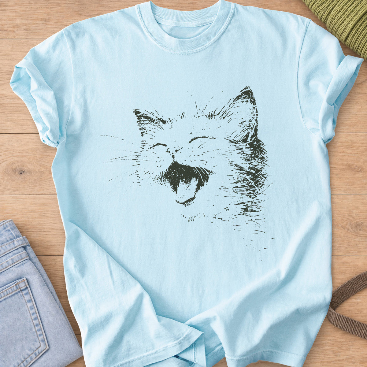 Cat laughing with eyes squeezed shut, mouth wide open and long whiskers, dark charcoal ink on a Chambray T-Shirt