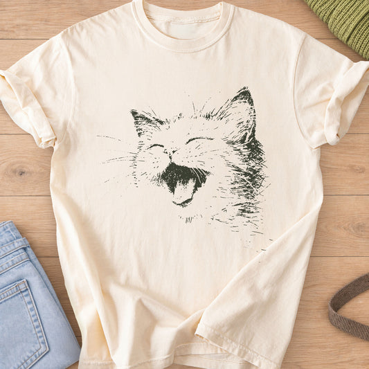 Cat laughing with eyes squeezed shut, mouth wide open and long whiskers, dark charcoal ink on an Ivory T-Shirt