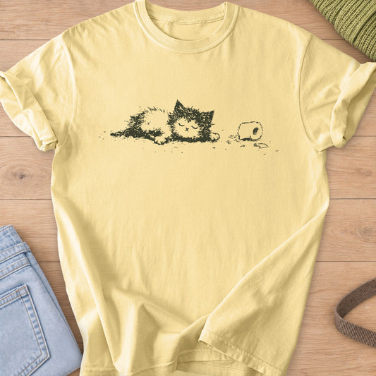 Fluffy cat napping with eyes closed beside a toilet paper roll and scattered shreds, dark charcoal ink on a Butter T-Shirt
