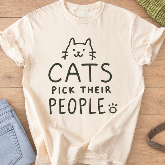 Simple cat face peeking over the words "Cats pick their people" and a paw print, dark charcoal ink on an Ivory T-Shirt