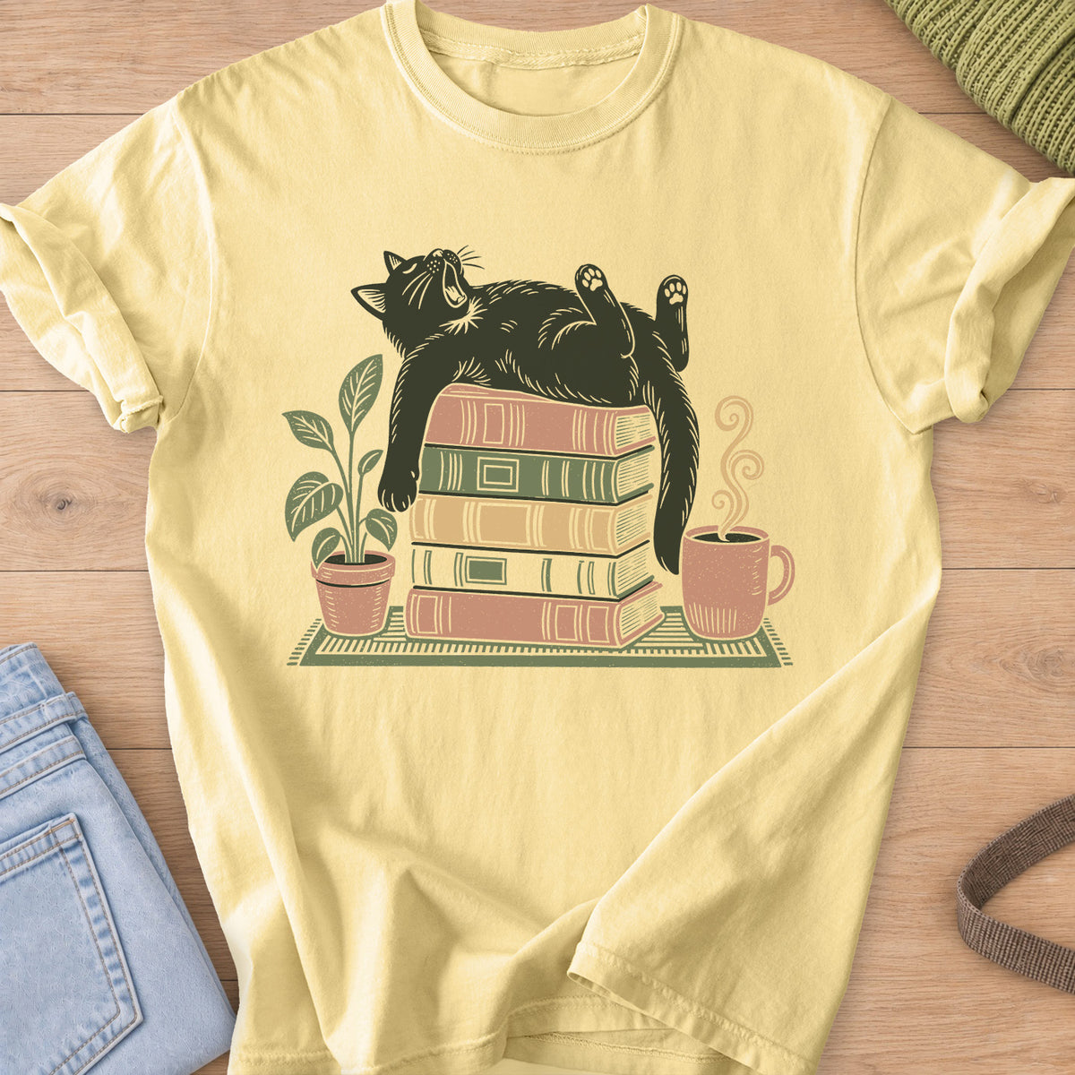 Cat yawning on its back on a stack of books by a potted plant and steaming mug on a Butter T-Shirt