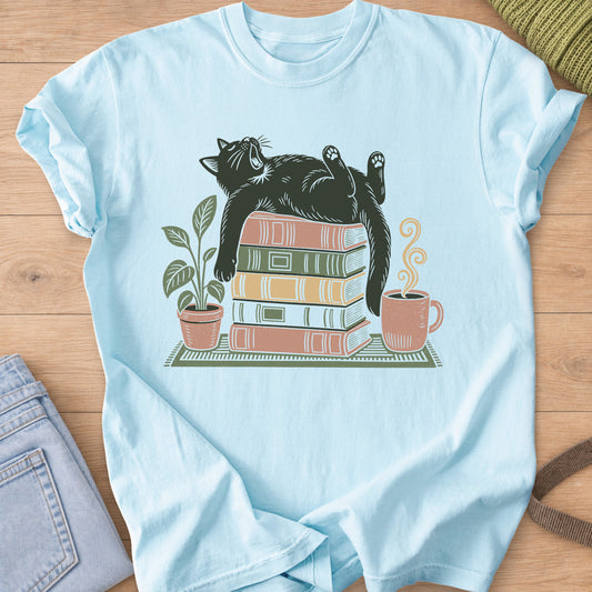 Cat yawning on its back on a stack of books by a potted plant and steaming mug on a Chambray T-Shirt