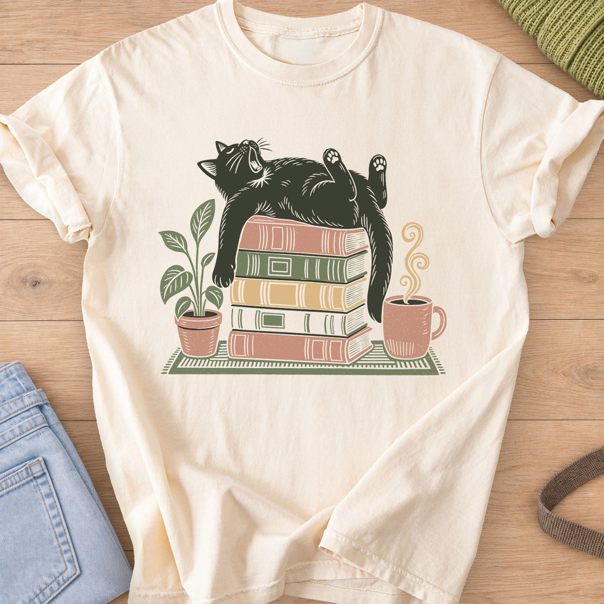 Cat yawning on its back on a stack of books by a potted plant and steaming mug on an Ivory T-Shirt