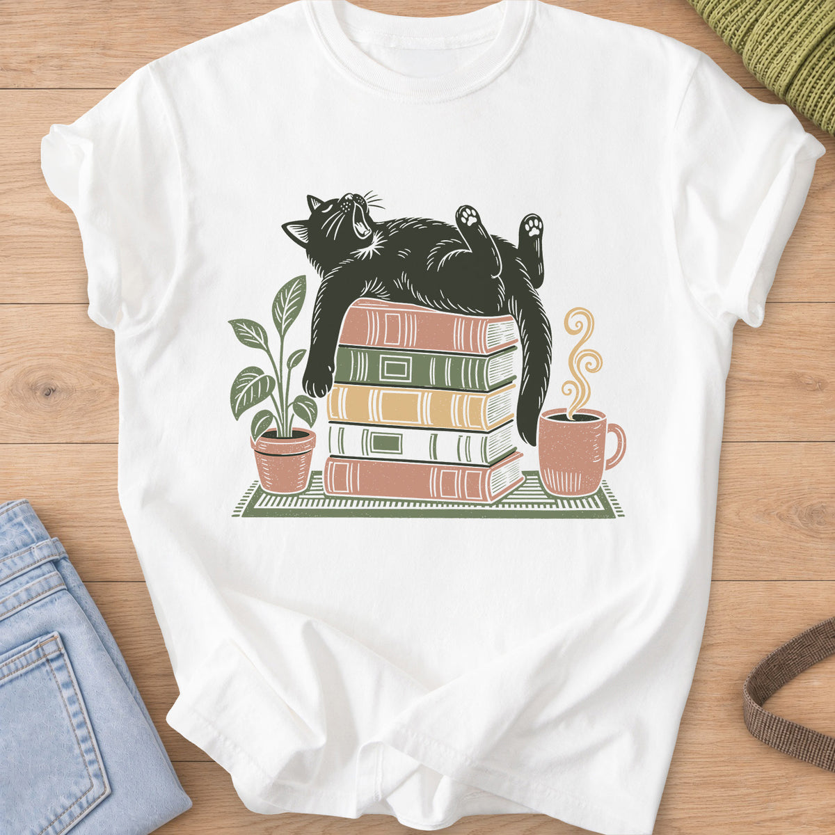 Cat yawning on its back on a stack of books by a potted plant and steaming mug on a White T-Shirt