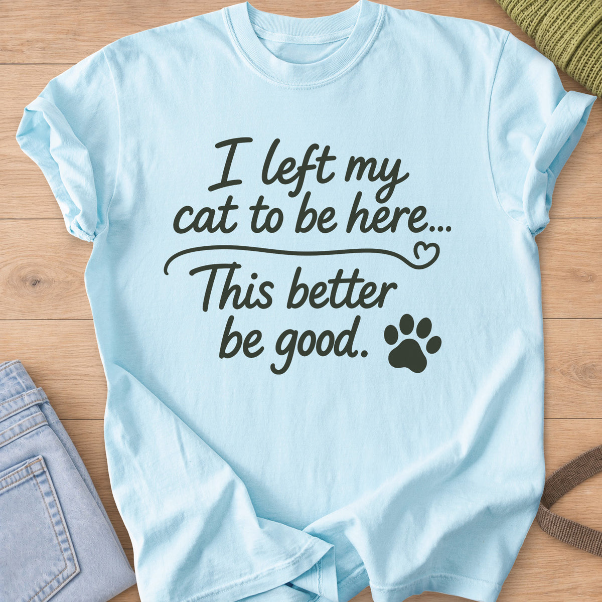 Script text "I left my cat to be here... This better be good." with a paw print, dark charcoal ink on a Chambray T-Shirt