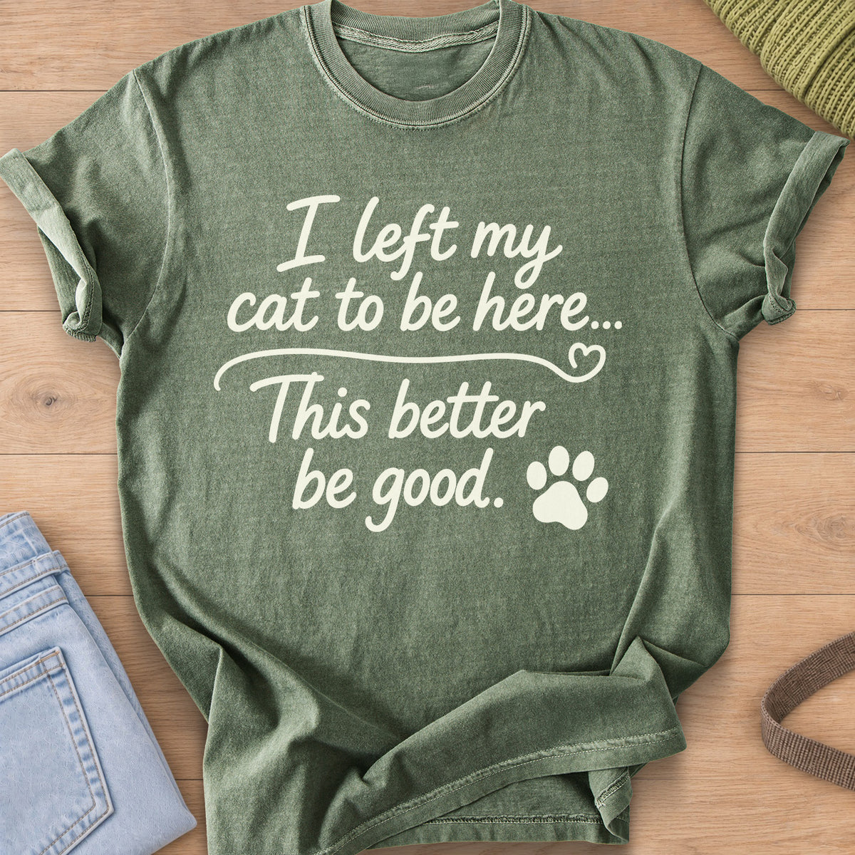 Script text "I left my cat to be here... This better be good." with a paw print, cream ink on a Moss T-Shirt