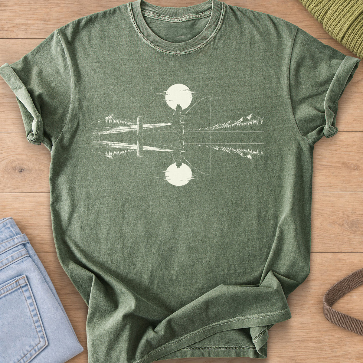 Cat silhouette fishing off a dock under a round sun, mirrored in a mountain lake, cream ink on a Moss T-Shirt
