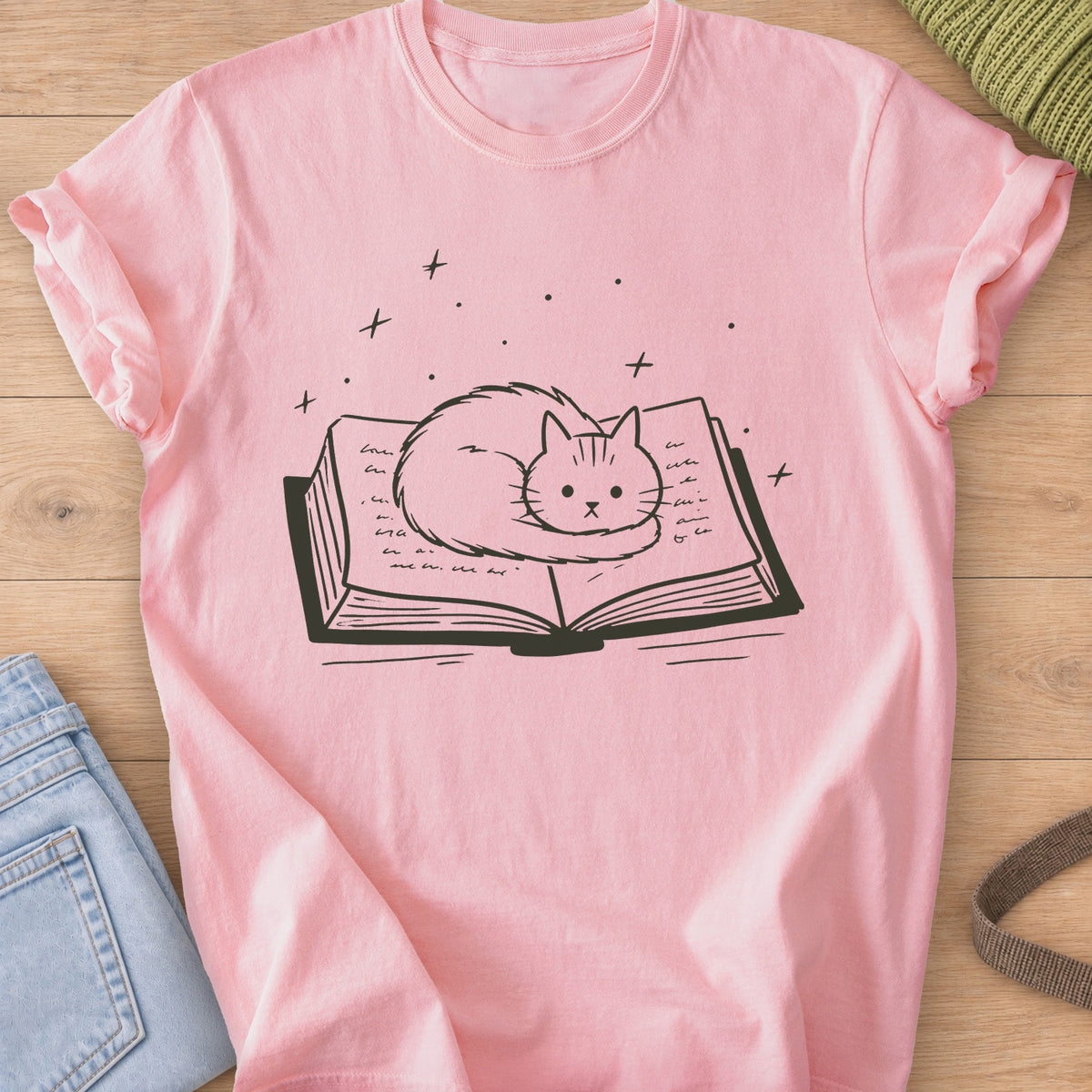 Fluffy cat curled up on an open book with sparkles and stars floating above, dark charcoal ink on a Blossom T-Shirt