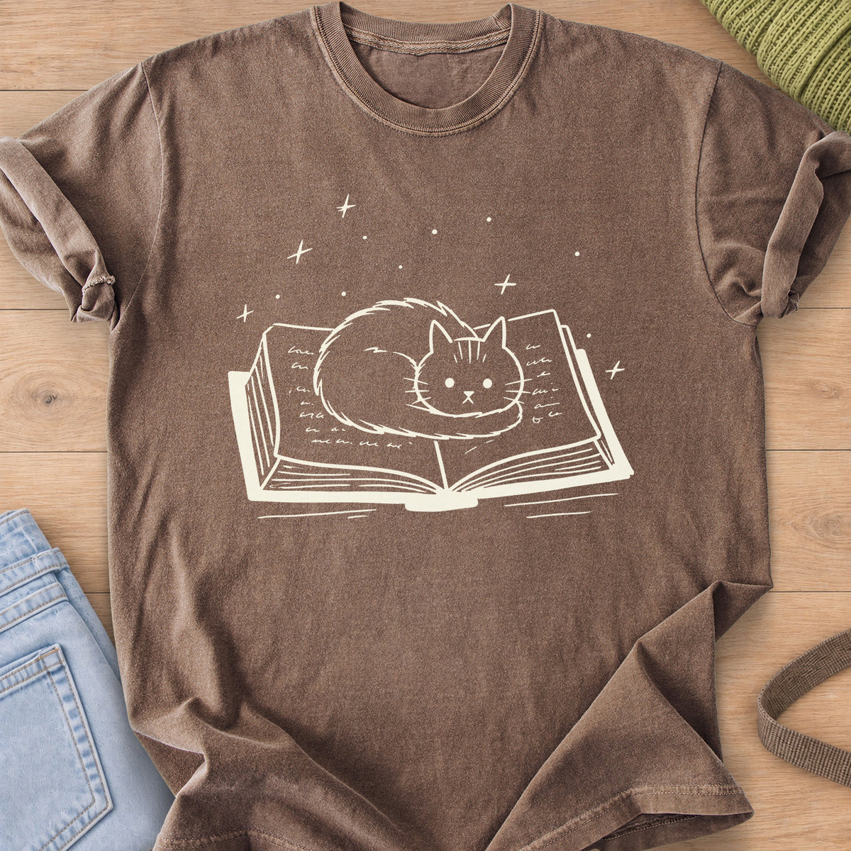 Fluffy cat curled up on an open book with sparkles and stars floating above, cream ink on an Espresso T-Shirt