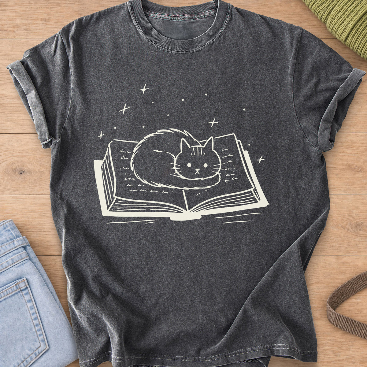 Fluffy cat curled up on an open book with sparkles and stars floating above, cream ink on a Pepper T-Shirt