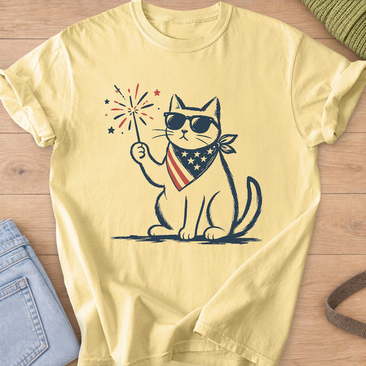 Sitting cat in sunglasses and a stars and stripes bandana holding a lit sparkler on a Butter T-Shirt